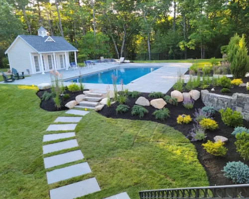 Landscape with walkway, many shrubs and plants, a backyard shed and a pool